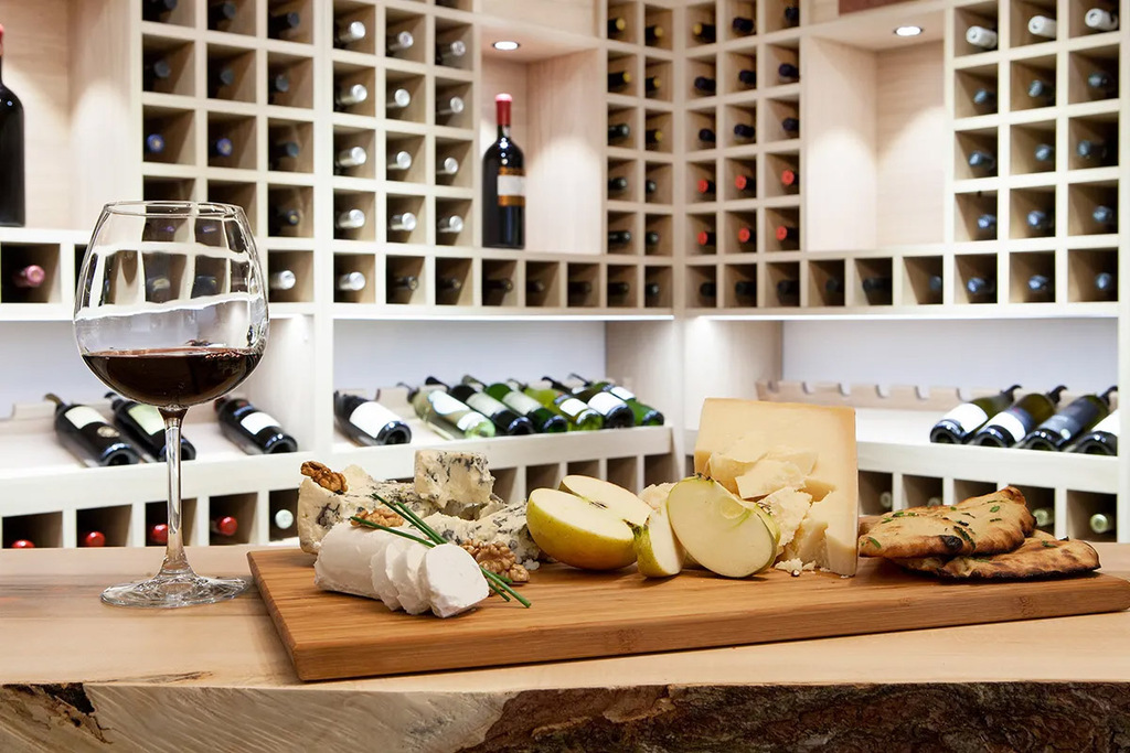 ワインセラーに陳列された数多くのワインボトルと、その手前に置かれたワイングラス、チーズ