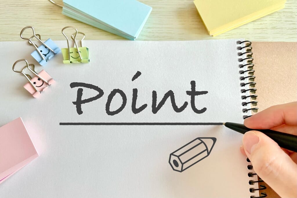 自宅での仕事効率UP！快適なワークスペースを作る5つのポイント　『Point』と書かれたノートに、ペンを持つ手が添えられた画像。カラフルなクリップや付箋が置かれ、重要なポイントを提示する場面を表現している。