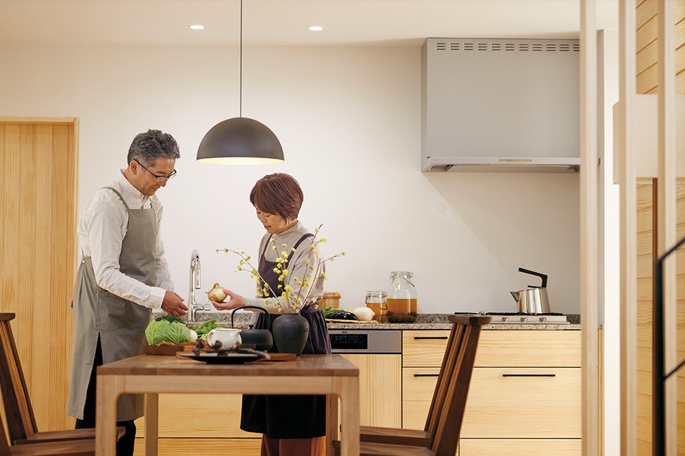 野菜を見つめる夫婦とウッドワンの壁つけキッチン