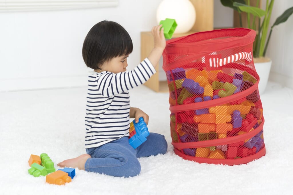 赤い収納袋におもちゃを片付ける子供