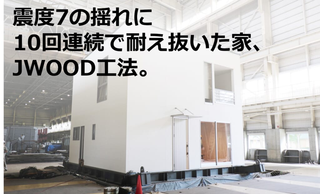 震度7の地震を再現する実験施設内で、白い小型の住宅モデルが揺れに耐えるためのテストを受けている様子。『震度7の揺れに10回連続で耐え抜いた家、JWOOD工法。』というテキストが画像を覆っている。