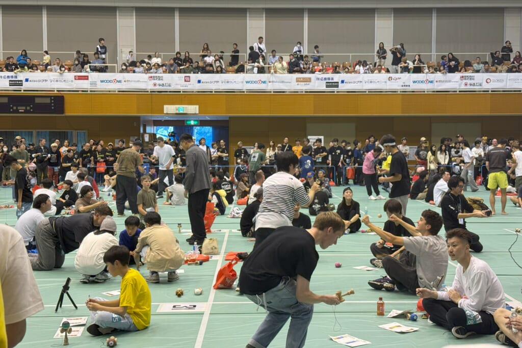 ウッドワンけん玉ワールドカップ2025の表彰台。大型スクリーンを背に、優勝トロフィーや賞金パネルを手にした選手たちが一堂に会している集合写真。