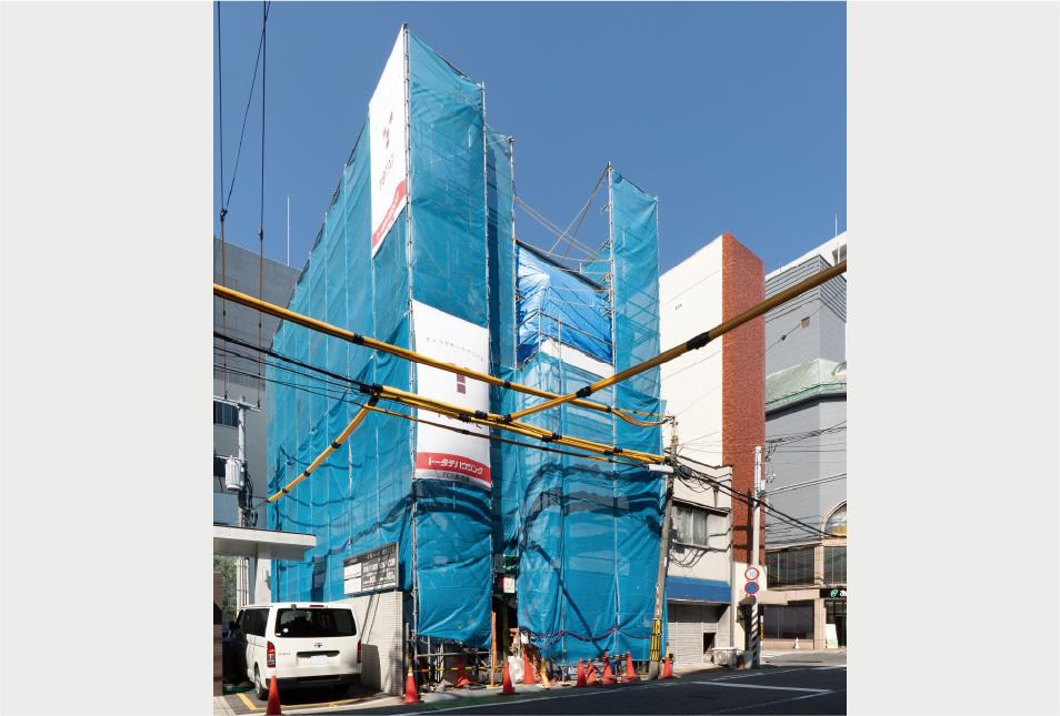 青い養生ネットに覆われた、建設中の木造4階建てビル。広島市中心部で進むプロジェクトの施工風景。